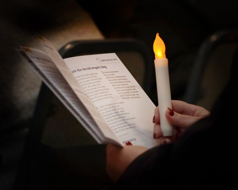 A woman's hands are shown in close up holding an order or service and lit artificial candle at the Light Up A Light Service