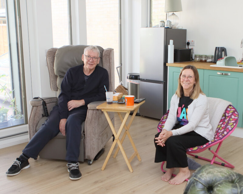 Richard is pictured seated in the living room of his new home alongside his wife Moira