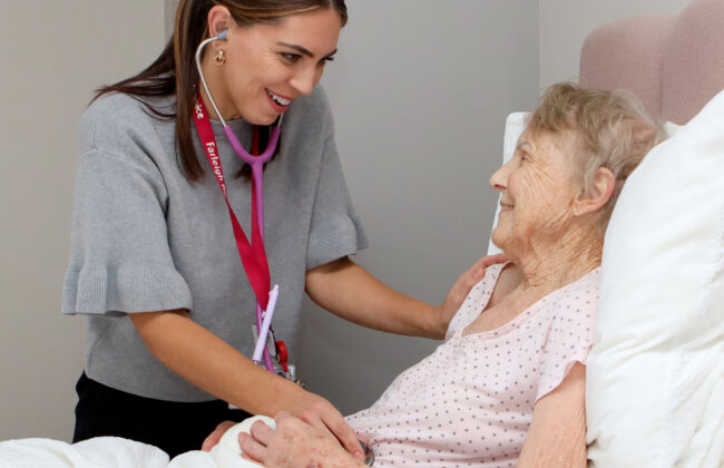 A Clinical Nurse Specialist gives care in a patients home, the patient is shown in bed interacting with a nurse