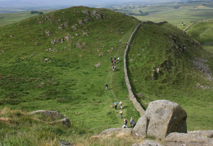 A group of diverse people walking together up a grassy hill under a clear blue sky.