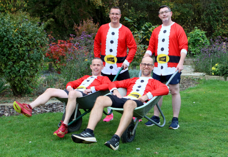 Four men from the Halstead Rockets running club pictures int eh Farleigh Garden wearing Santa tops, 2 are in wheelbarrows and two are pushing them