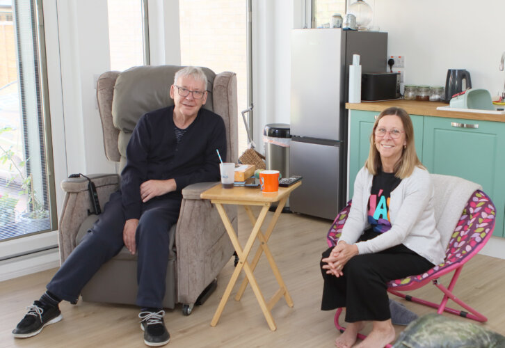 Richard is pictured seated in the living room of his new home alongside his wife Moira