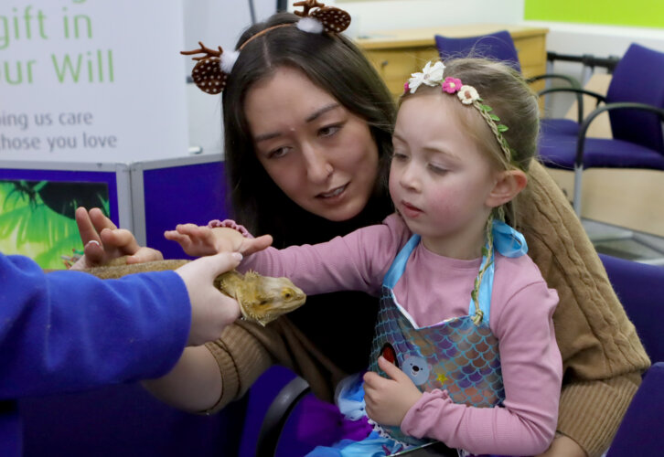 A mother and young female child stroke a bearded dragon lizard